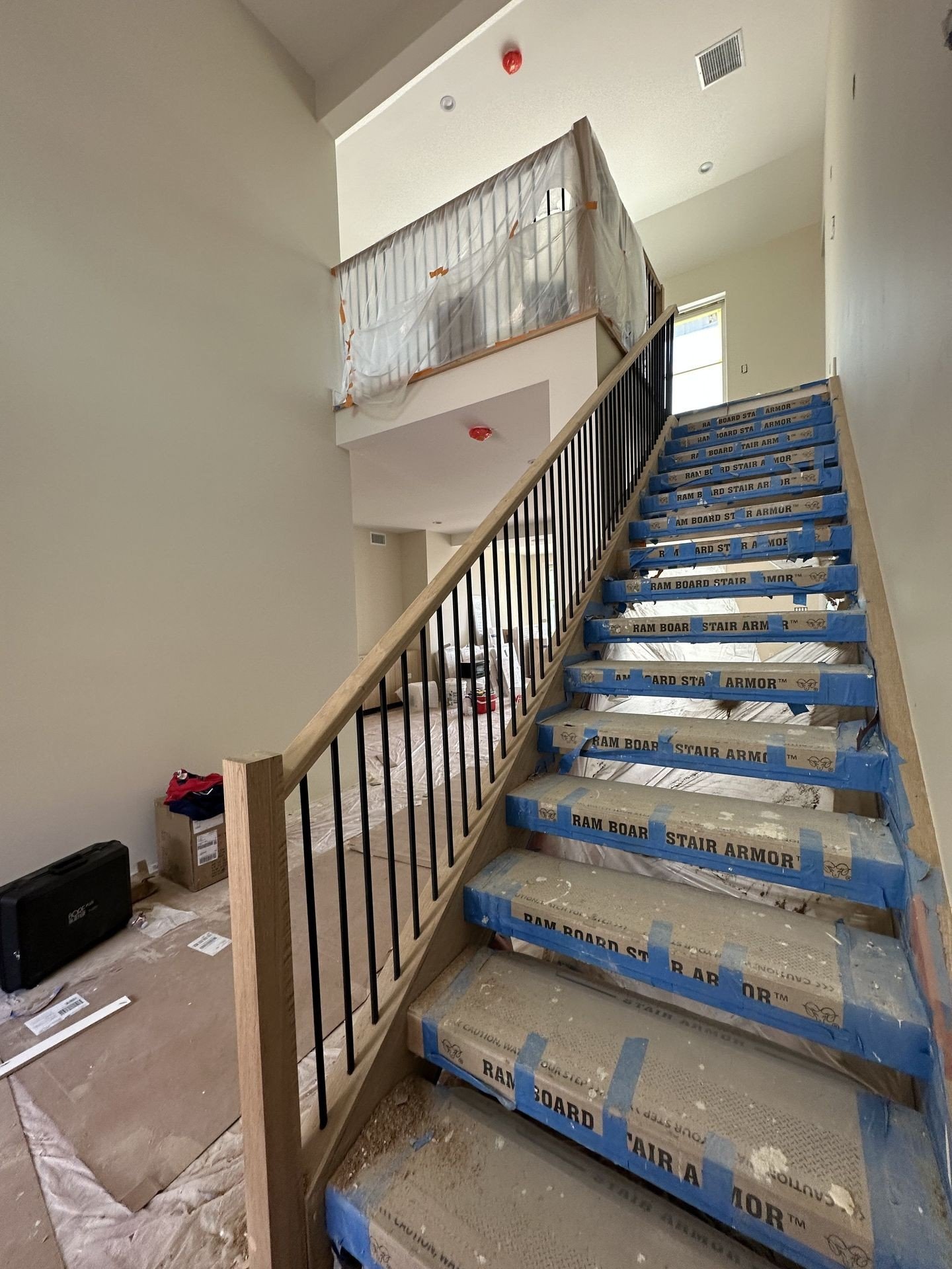 Staircase mid-conversion with protective covering over new hardwood treads and black metal balusters in a Los Angeles home